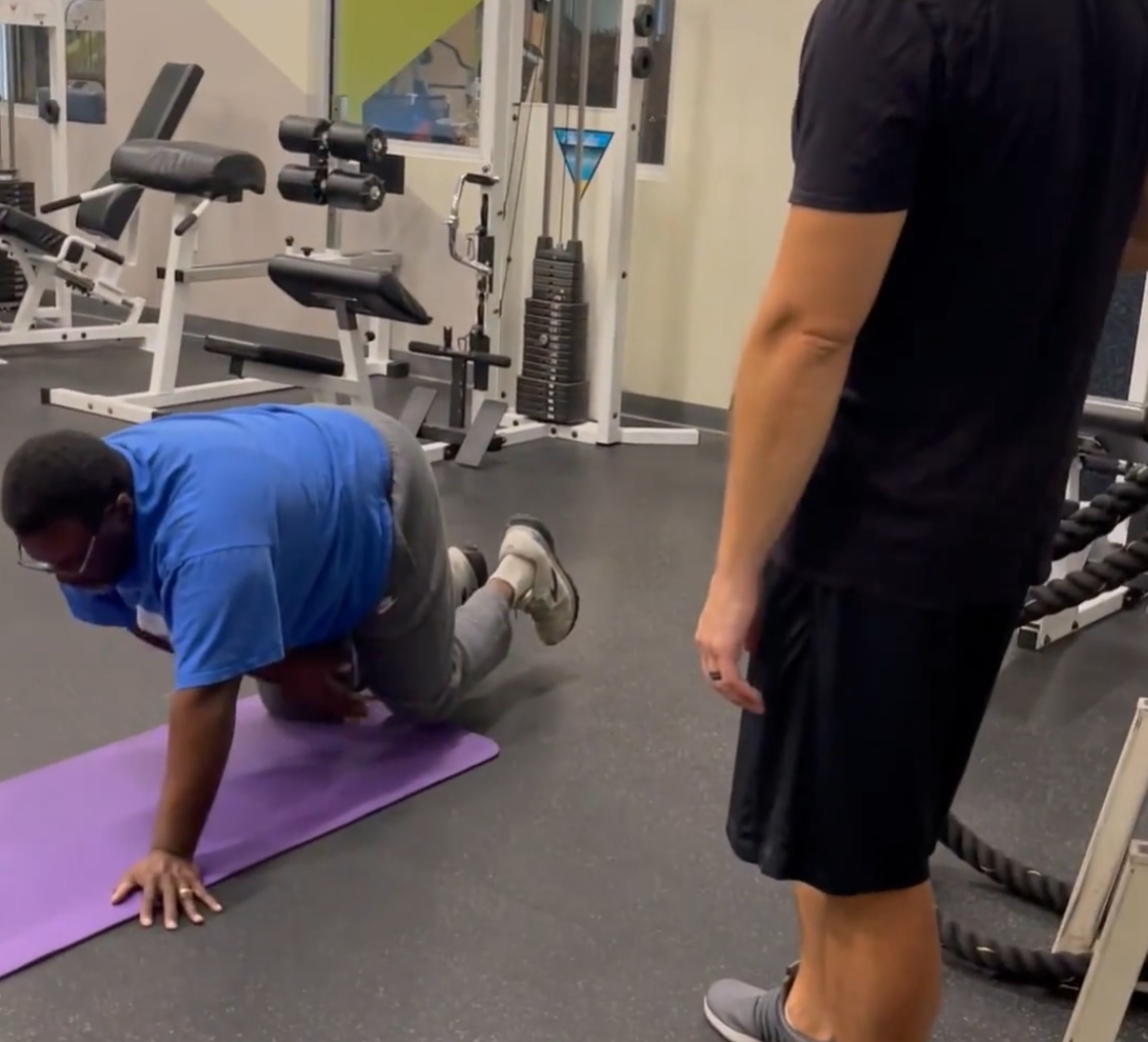 Ben doing floor exercises on mat with trainer coaching